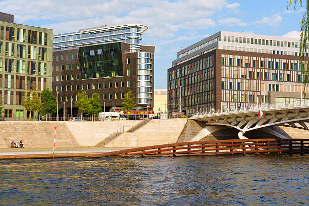 Berlin, Germany - August 20, 2025: Stunning view of contemporary buildings by the Spree River in Berlin, showcasing modern design elements, lush greenery, and visitors enjoying the waterfront.