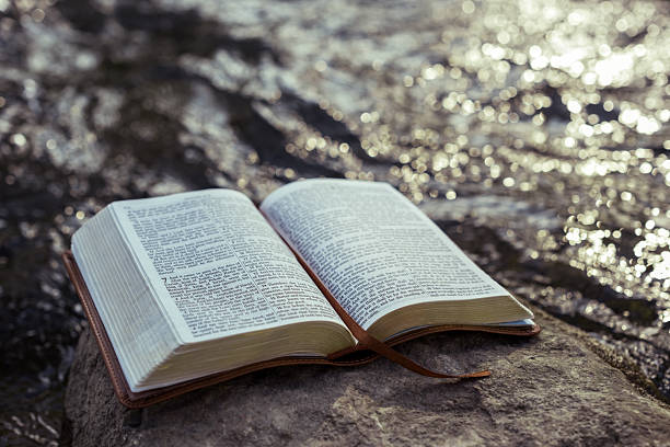 istock Open Bible on rock by flowing river 2235502989