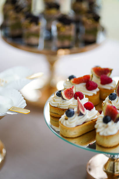 Mini cakes with cream and berries served on a mirror stand for a festive dessert table.