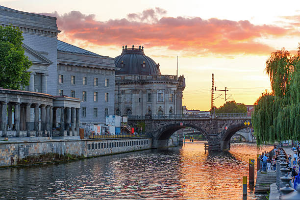 Berlin, Germany - August 17, 2025: Stunning sunset illuminating Berlin's historic buildings along the riverbank with reflections.