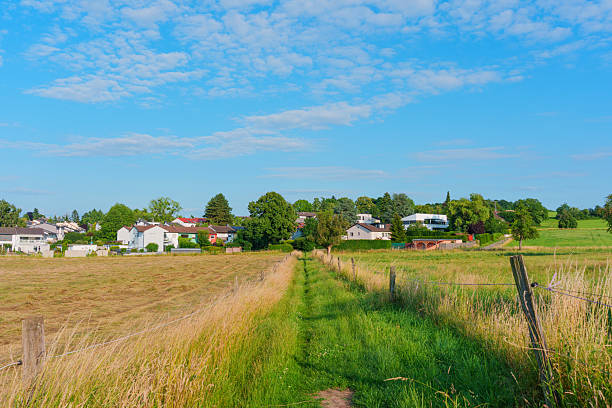 Scenic path bordered by tall grass leading to a quaint village under a clear blue sky in Rossdorf, Germany, showcasing rural charm and tranquility.