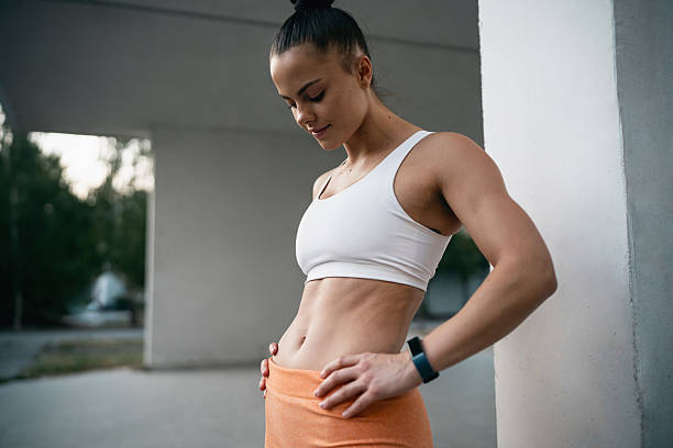 A sporty young woman outside, showing pride as she looks at her abs.
