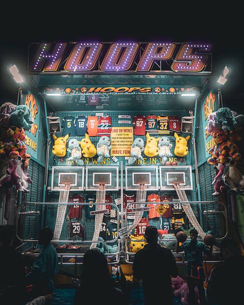 Toronto, Canada – August 27, 2023: Carnival basketball game booth at night with colorful stuffed toys and jerseys, people playing in the foreground.