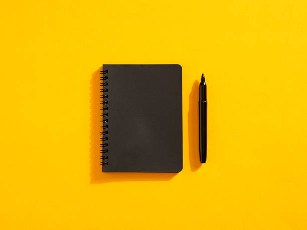 istock Black notebook and pen resting on a vibrant yellow background 2235507945