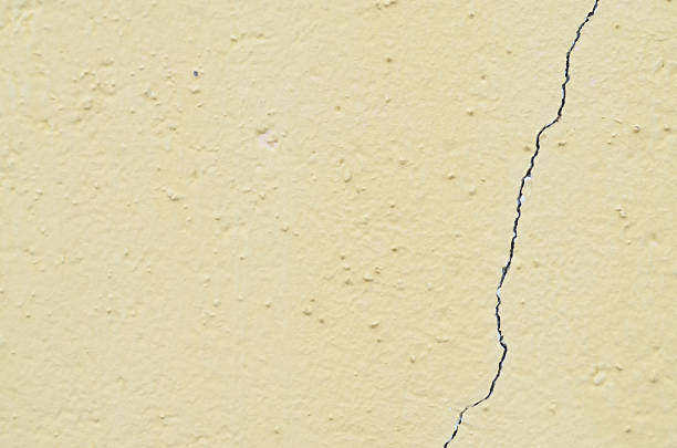 vertical crack runs along a weathered, pale yellow wall, effectively illustrating the need for repair, maintenance, and home improvement.