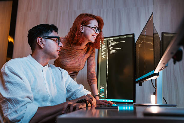 istock Two colleagues collaborate at dual monitors in a modern office, reviewing code on screens and discussing software development. 2235509513