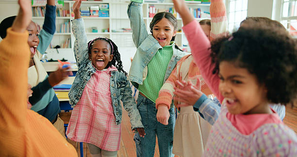 istock Children, excited or hands raised in celebration in classroom for recess, learning or end of school. Students, group and happy people at montessori with study break, education and development goals 2235513589