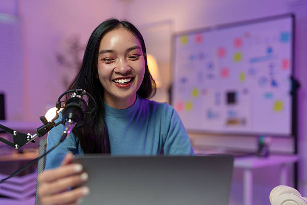 istock Cheerful young asian woman using professional microphone and laptop, broadcasting live, recording podcast, or making video call at home office 2235513836