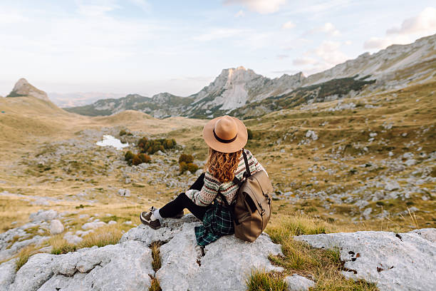 istock A young female hiker with a backpack and hat sits on a rock, looking at the mountain scenery. 2235517483