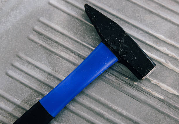 Close-up of a black hammer with a blue handle resting on a metal surface