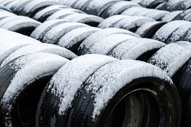 Stack of old used bus vehicle tires covered in winter snow, selective focus