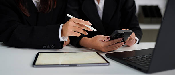 istock Two colleagues discussing data with smart phone and new modern computer laptop on desk table. Close up business team concept. 2235523485