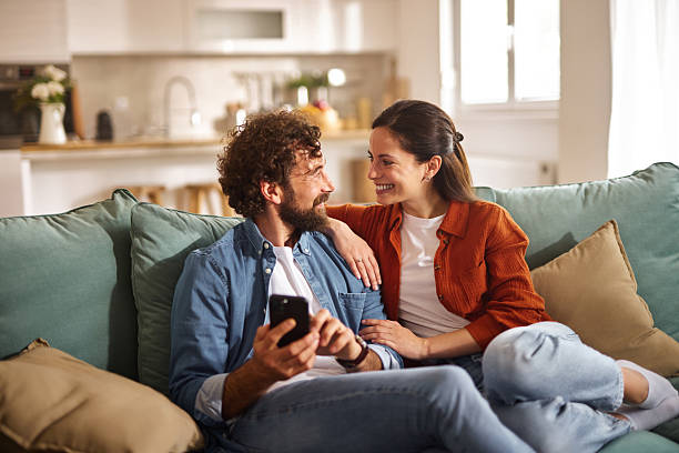 istock Happy couple relaxing on sofa, browsing internet on smartphone at home 2235524870