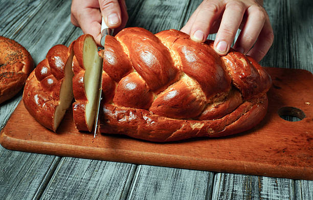 istock Hands carefully slice into a golden-brown challah bread resting on a rustic wooden cutting board. The warm bread exudes inviting aromas, perfect for any meal 2235525918