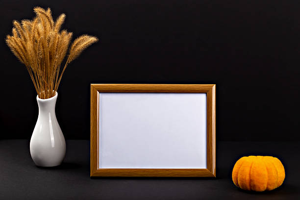 istock Decorative autumn arrangement with empty frame, orange pumpkin, and dried grass on dark background 2235529284