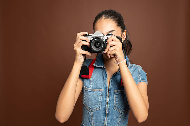 istock Woman holding retro camera up to face in studio with brown background horizontal 2235529342