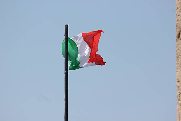 Close-up of the Italian national flag, tricolour green, white, and red, waving on a flagpole against a bright clear blue sky. Symbol of Italy and Italian identity, photographed outdoors on a sunny day.