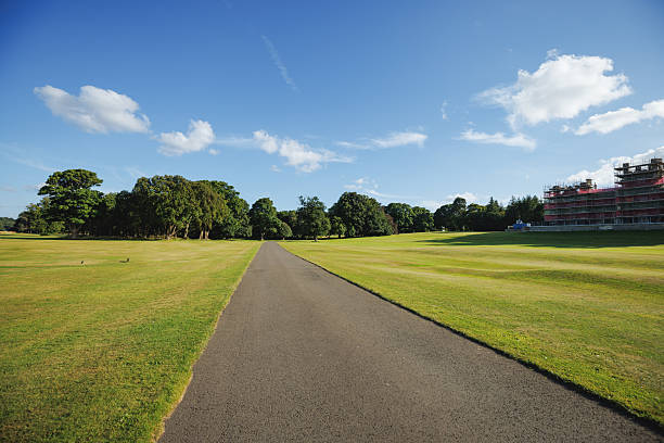 A sunny day scene featuring a paved pathway traversing vast green fields, bordered by trees and distant buildings. The tranquil setting embodies outdoor serenity and highlights the scenic beauty of Edinburgh.