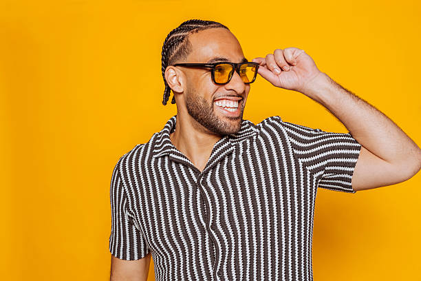 istock Smiling young man with braids touching sunglasses on yellow background 2235536927