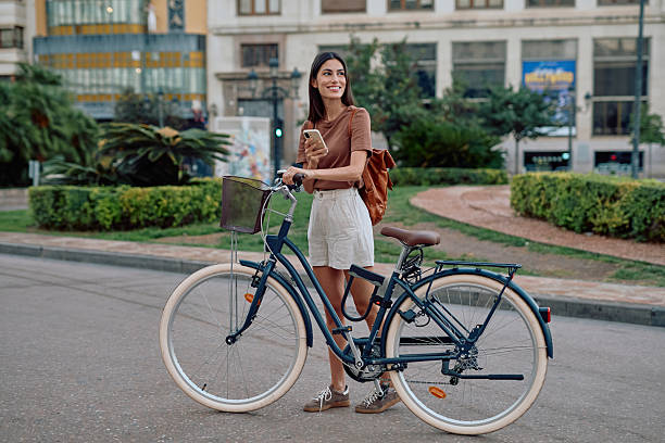 istock Young woman using smartphone while holding her bicycle in the city 2235537270