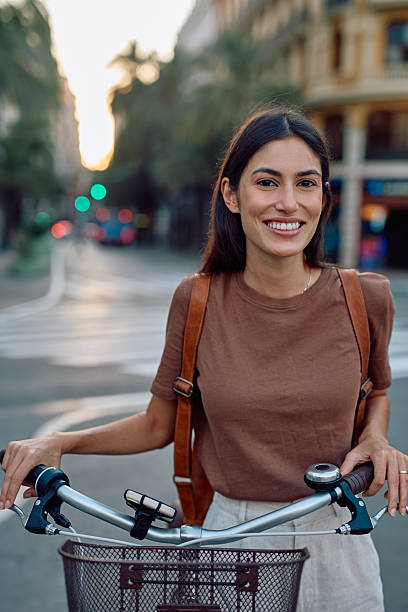 istock Young woman smiling while holding her bicycle in the city 2235537437