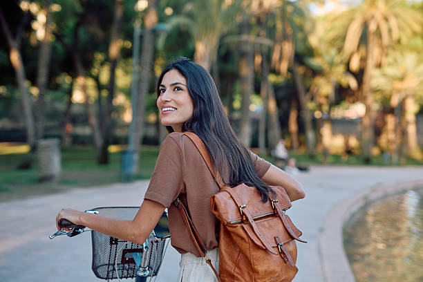 istock Young woman walking with her bicycle in a park looking back over her shoulder 2235537509
