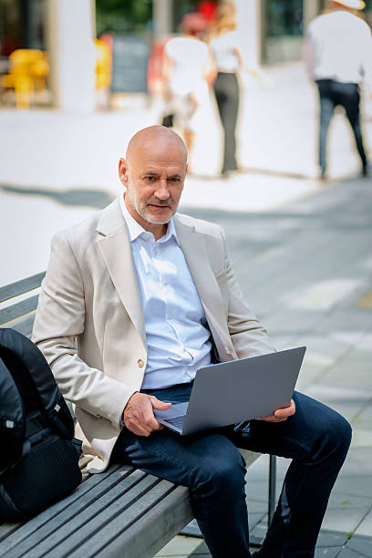 istock Business man sitting outdoors in the city and using his laptop computer 2235537699