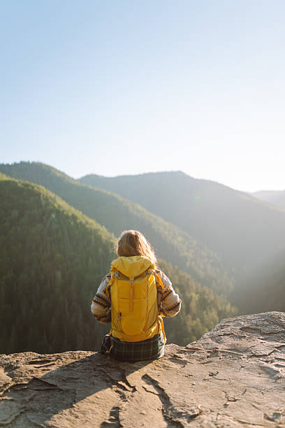 istock A female hiker with a bright yellow backpack sits on a cliff and looks at the mountain range. 2235538286