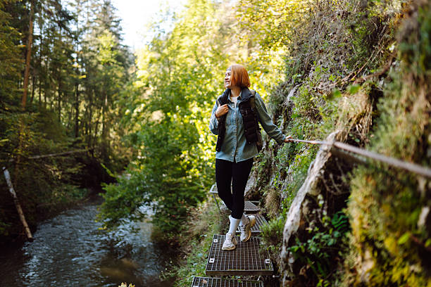 istock Beautiful female hiker with backpack standing on metal walking path near stream.  Active lifestyle. 2235540216