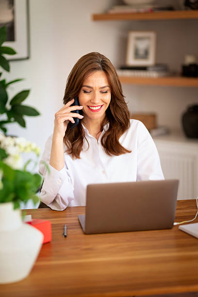 istock Middle aged attractive woman sitting in her modern home and using laptop computer and smartphone 2235540274