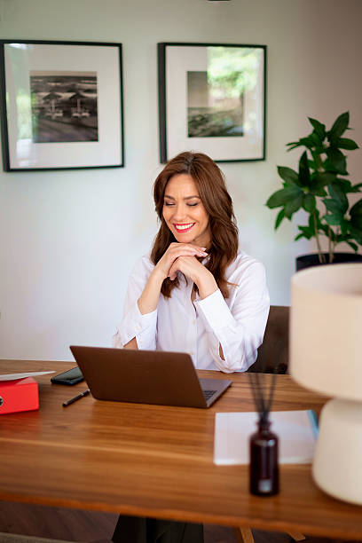 istock Middle aged woman sitting in her modern home and using laptop computer 2235540329