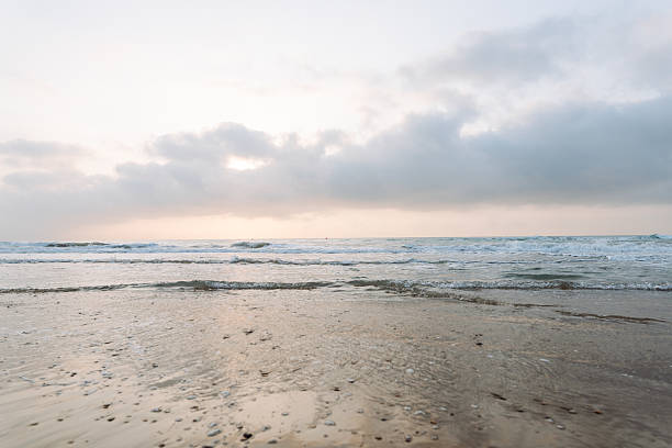 istock Seascape. Soft waves roll onto a sandy beach as the sun sets in the background. 2235540756