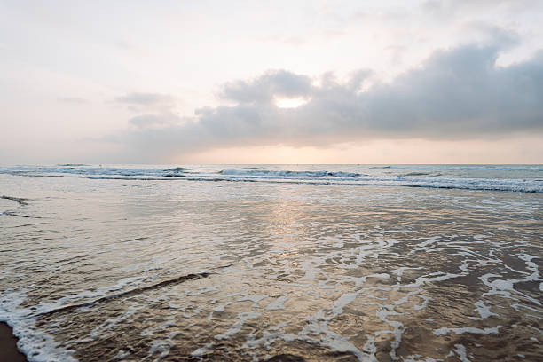 istock Seascape. Soft waves roll onto a sandy beach as the sun sets in the background. 2235540814