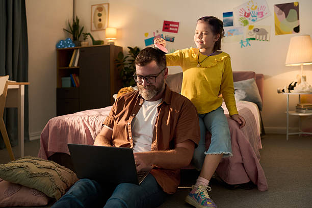 istock Middle Aged Man Using Laptop While Child Girl Playing Behind Him 2235541191