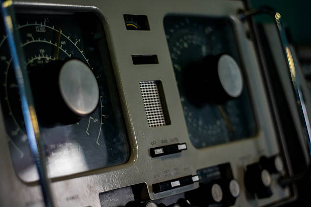 Old maritime navigation equipment featuring analog dials, meters, and knobs. The dials have circular scales with numerals, possibly for speed or direction, and the device includes several switches or buttons below the main controls. The equipment is housed in a metallic casing with handles on the sides, indicating it was part of a ship's control panel. The design reflects technology from a past era of maritime navigation.