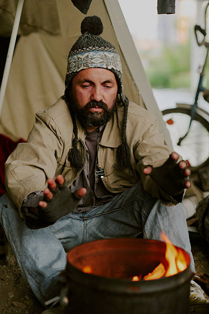 istock Homeless Caucasian Man Warming Hands by Campfire Outdoors near Tent 2235543775