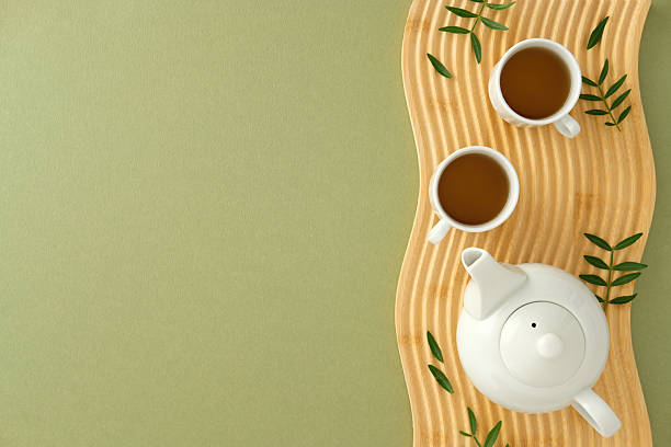 istock Minimalist tea ceremony setup with white ceramic teapot and cups on a wavy wooden tray, accented by green leaves 2235544501