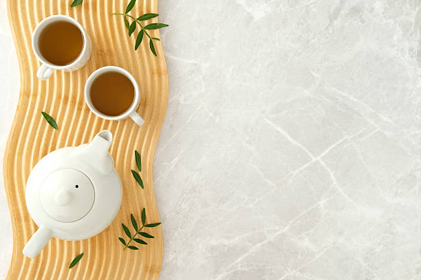 istock Elegant tea setting with white teapot and cups on wavy wood tray on marble table 2235544598