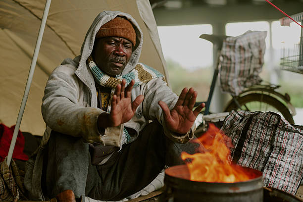 istock Homeless Black Man Warming Hands by Fire Outdoors under Makeshift Shelter 2235545974