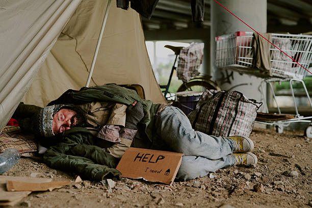 istock Homeless Caucasian Man Sleeping Outdoors under Bridge Holding Help Sign 2235547533