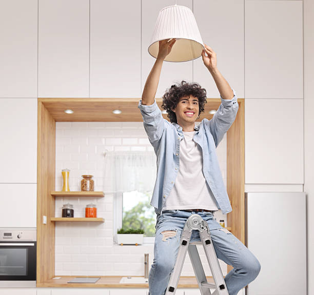 istock Young man on a ladder and changing a light bulb 2235548601