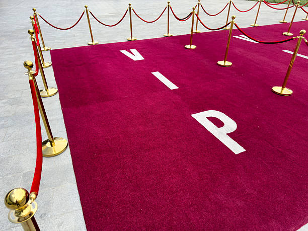 A red carpet leads to a large golden star, with gold stanchions and red velvet ropes lining the sides of the carpet. The background is a backdrop of red curtains.