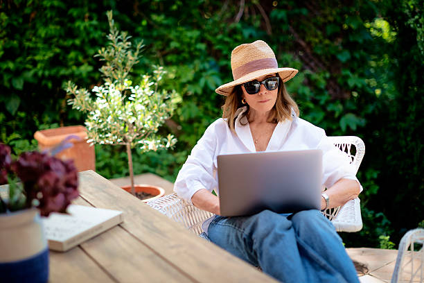 istock Attractive female wearing sunhat and casual clothes while sitting outdoor and using her laptop computer 2235552311