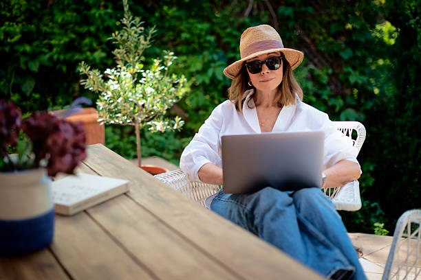 istock Mature woman sitting outdoor in back yard and using a computer laptop 2235552318