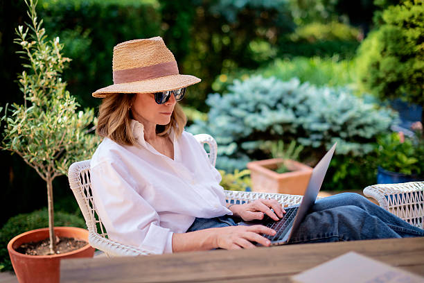 istock Attractive female wearing sun hat and casual clothes while sitting outdoor and using her laptop computer 2235552323