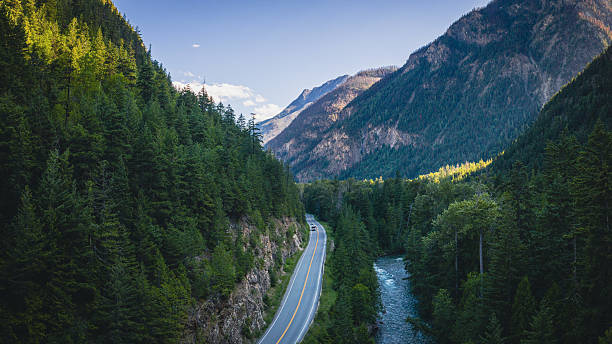 Aerial view of a scenic road trip along the Sea to Sky Highway (Highway 99) near Lillooet, British Columbia, Canada. The winding mountain road follows a fast-flowing river through dense evergreen forests and rugged peaks. This dramatic landscape captures the essence of Canada travel, freedom, and adventure on one of the country’s most iconic scenic drives.