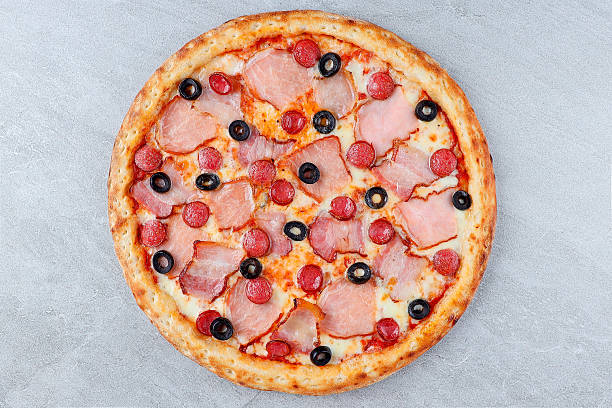 istock Pizza with Ham, Mini Pepperoni Slices, Black Olives, and Melted Cheese on Crispy Crust over Gray Stone Background 2235554896