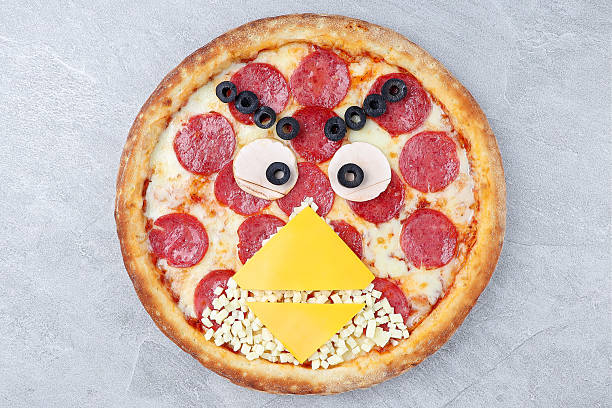 istock Creative Angry Birds Style Pepperoni Pizza Decorated with Cheese Beak, Ham Eyes, and Olive Details on Gray Stone Background 2235554981