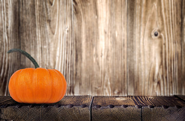 Bright orange pumpkin sits on a weathered wooden table, surrounded by a rustic wooden background, evoking a warm autumn atmosphere and seasonal charm