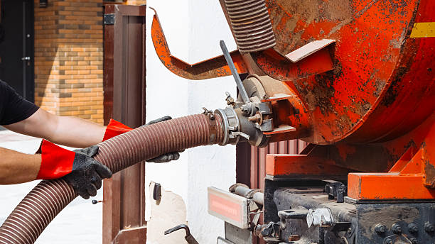 Technicians operate a vacuum truck to service a septic tank at a home, ensuring proper sanitation. Septic tank service. Sewage Tank truck.